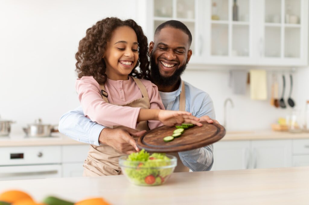 Cheerful afro father and daughter cooking salad together